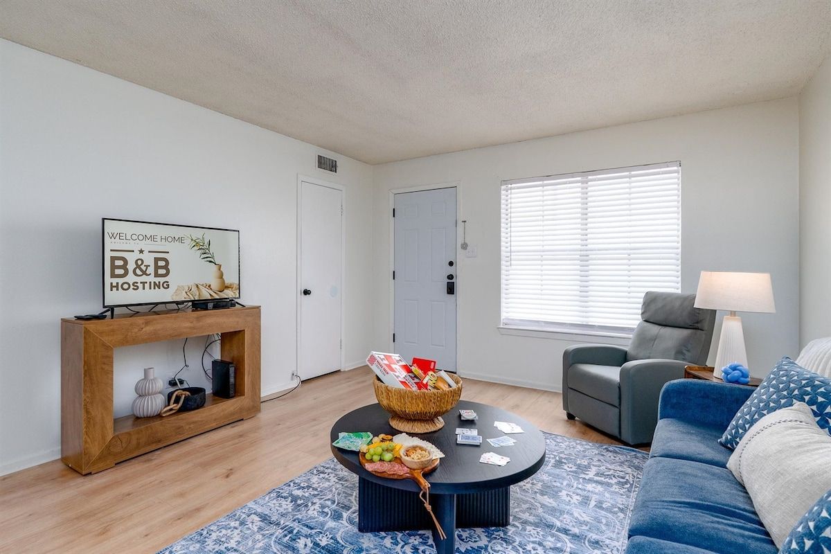 Un salon comprenant un canapé, une table basse avec un panier, une console sur laquelle est posé un panneau, et une porte.