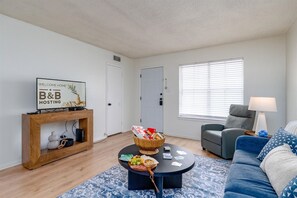 A living room with a sofa, a coffee table with a basket, a console table with a sign, and a door.