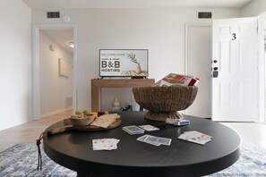 A round table with playing cards, a bowl, and a welcome sign in a room with a white door and a framed picture on the wall.