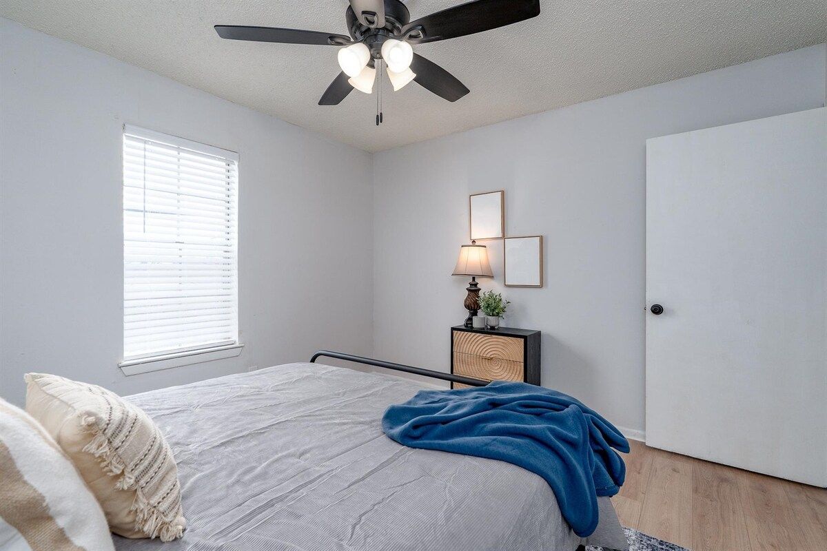A bedroom with a bed, a ceiling fan, a bedside table with a lamp, and a door.