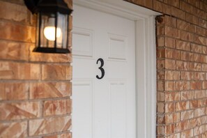 A white door with the number '3' above it, set in a brick wall.