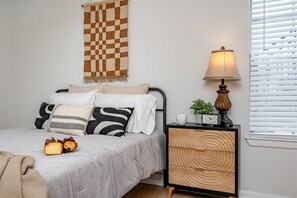 A bedroom with a bed, bedside table, lamp, and a checkered wall hanging.