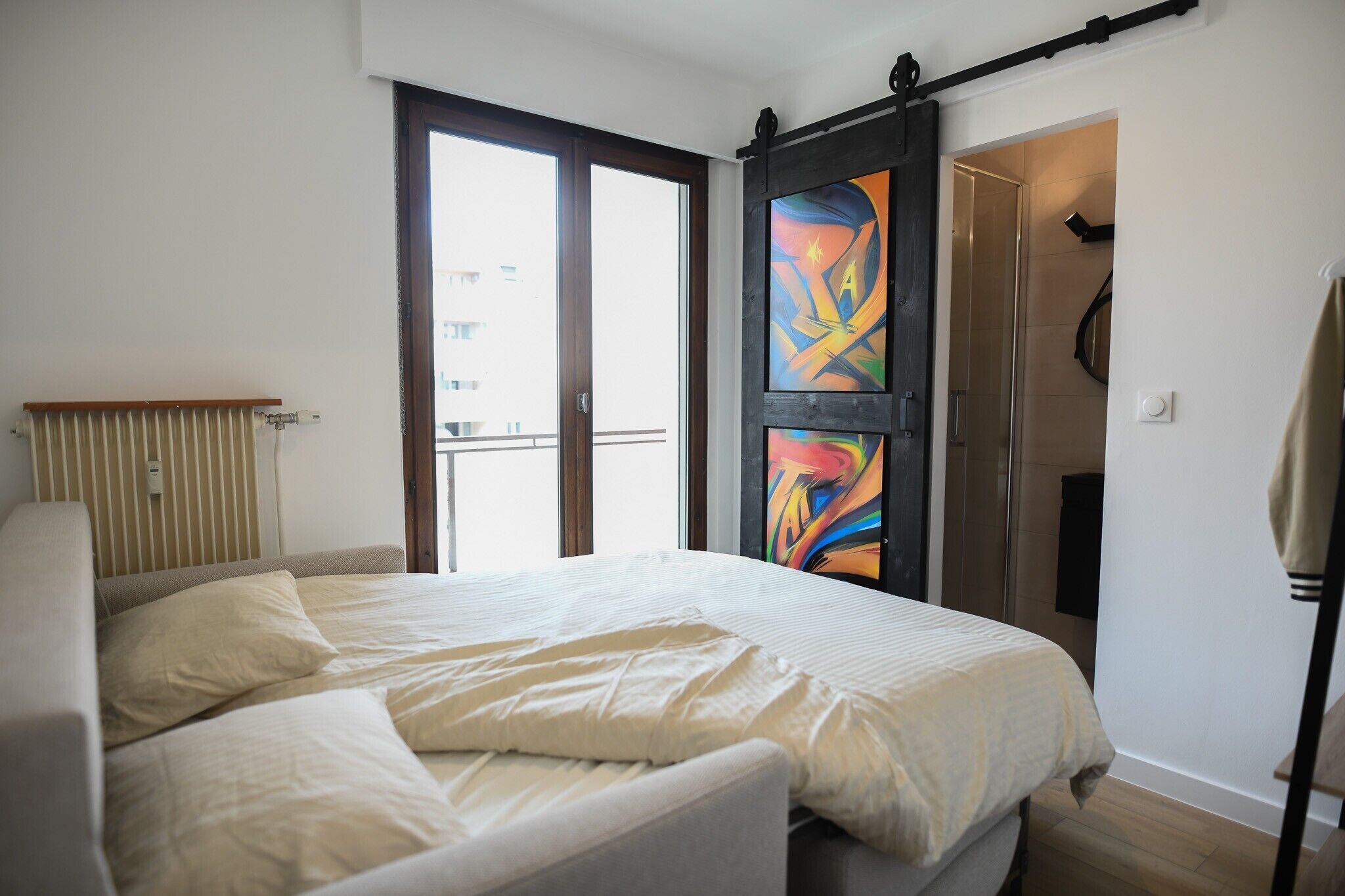 A bedroom with a bed, a radiator, a window, and a door with a sliding mechanism.