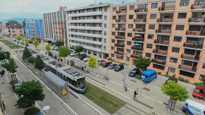A multi-story building with balconies, a tram line, and parked cars.