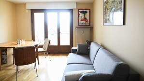 Una sala de estar con un sofá, una mesa de comedor con sillas, un radiador y una ventana con vistas.