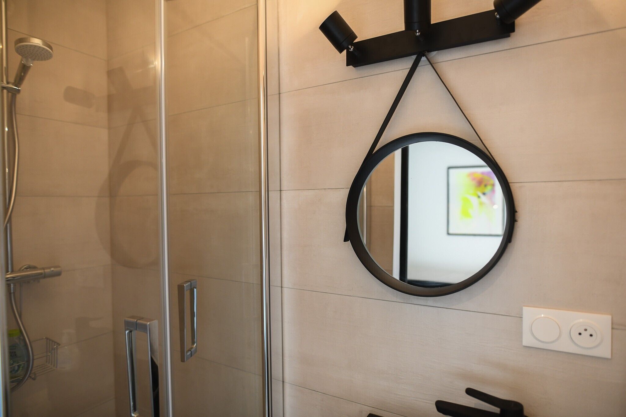 Une salle de bain avec une douche à parois de verre, un miroir rond et un luminaire fixé au mur.