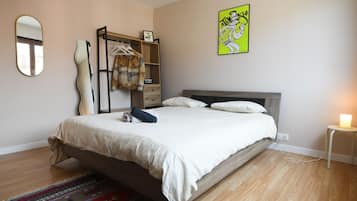 A bedroom with a bed, a bedside table with a lamp, a dresser, a mirror, and a wall art piece.