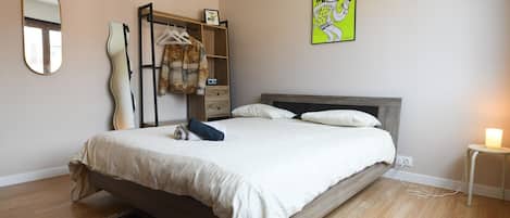A bedroom with a bed, a bedside table with a lamp, a dresser, a mirror, and a wall art piece.