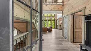 A spacious hallway with wooden flooring and a high ceiling, leading to a seating area with a view of greenery outside.