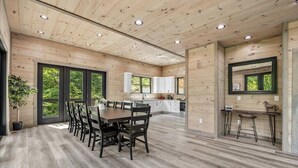 A spacious kitchen with wooden cabinets, a dining area with a table and chairs, and large windows offering views of greenery.