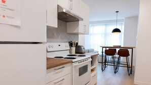 A modern kitchen with white cabinetry, a built-in oven, a stove, and a dining area with a table and chairs.