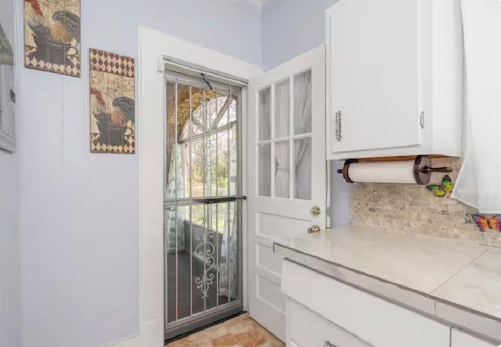 Una cocina con gabinetes blancos, una puerta de vidrio y un salpicadero de azulejos.