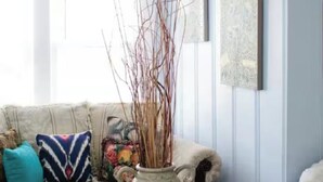 A living room with a glass coffee table, a sofa with colorful cushions, and a vase with branches.