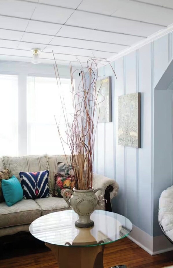 Un salon avec une table basse en verre, un canapé agrémenté de coussins colorés et un vase décoré de branches.
