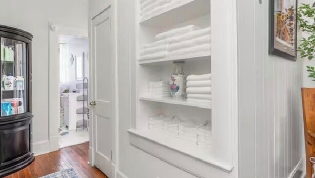 A hallway with a white closet containing folded towels and a decorative vase.