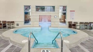 An indoor swimming pool with a tiled deck, a clock on the wall, and chairs around the pool area. - Westwinds - Funky Basecamp in the Rockies (Canmore)
