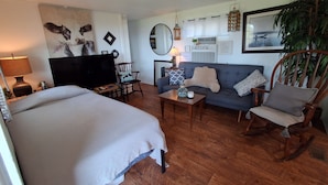 Una habitación bien amoblada con cama, sof á y mecedora, televisión y una pared decorada.