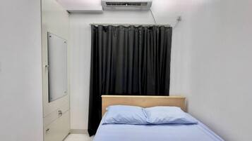 Un dormitorio pequeño y moderno con una cama individual, un armario y una ventana con cortinas negras.