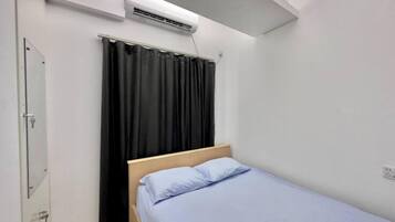 Una habitación pequeña con una cama individual, cabecera de madera, cortina negra y un equipo de aire acondicionado en la pared.