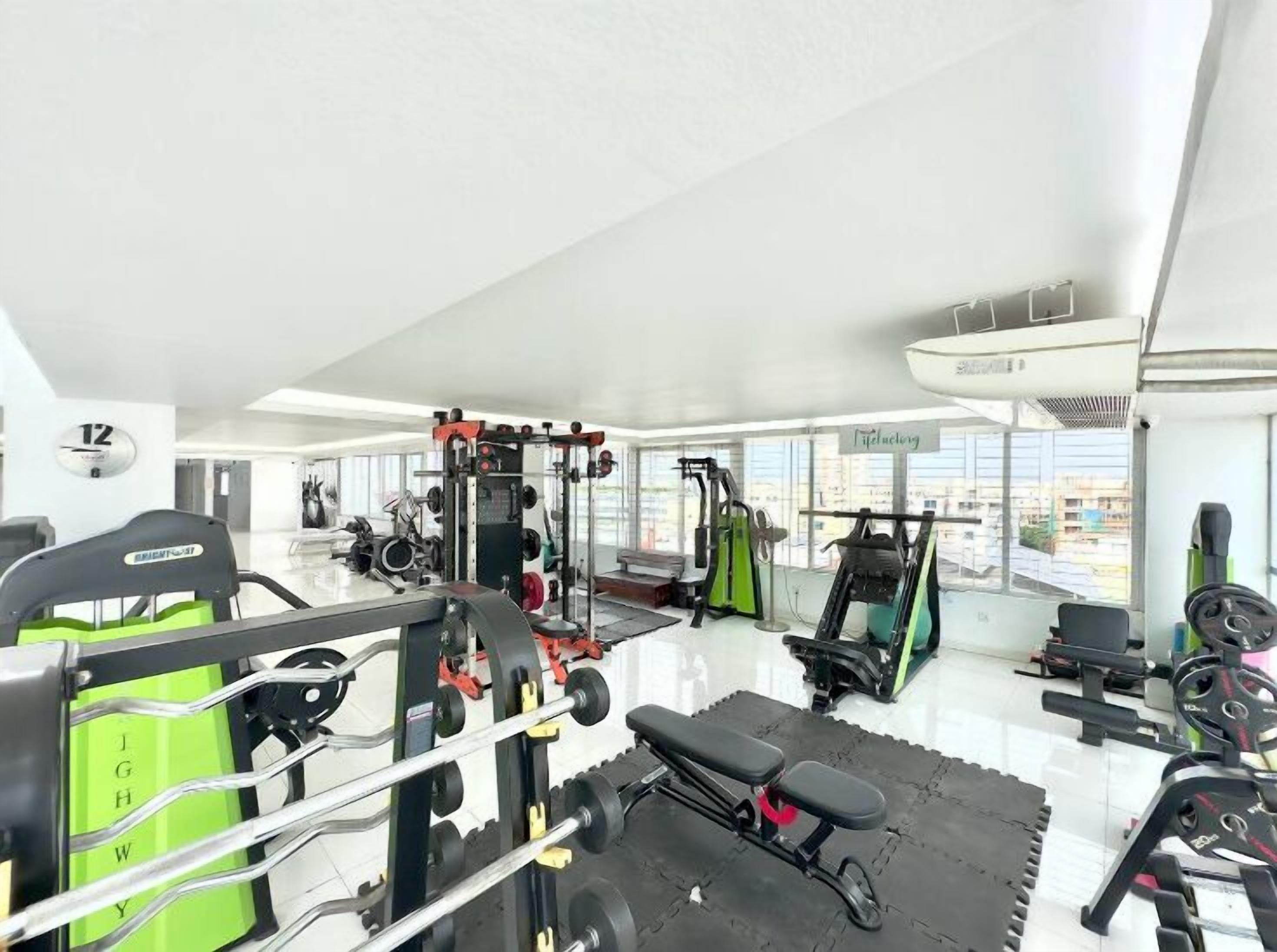A gym with various exercise equipment, a bench, and a large window offering a view of the city.