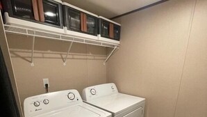 Et vaskerum med to hvide vaskemaskiner, en beige måtte og en kost.