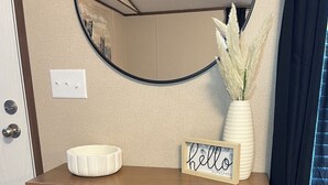Et trækonsolbord med en hvid skål, et skilt med ordet 'hello' og en vase med tørrede planter. To flettede kurve står under bordet.