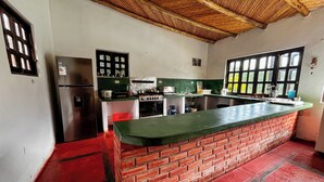 Une cuisine avec un comptoir en briques, un réfrigérateur, une cuisinière et une fenêtre équipée de stores.