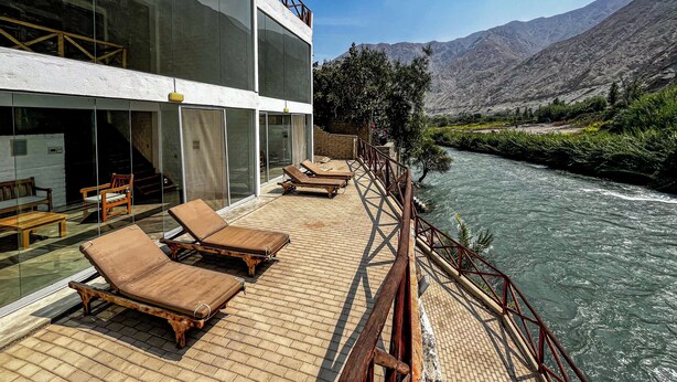 Un bâtiment moderne doté de grandes fenêtres en verre, d’une terrasse en bois avec des chaises longues et offrant une vue sur la rivière.