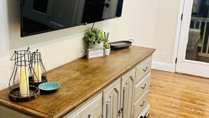A living room with a wooden cabinet, a flat-screen TV, and a small plant on the cabinet.