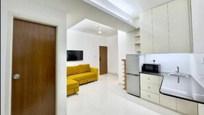 Una cucina moderna con mobili bianchi, un forno a microonde e un lavello. Nell'area soggiorno adiacente, c'è un divano giallo.