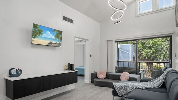Una sala de estar moderna con un ventanal grande, un televisor integrado y un sofá gris con cojines decorativos.