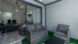 Una sala de estar moderna con un sofá gris, dos sillas de mimbre, un cerramiento corredero de vidrio y un ventilador de techo.