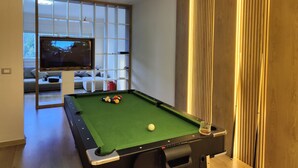 Uma mesa de bilhar com bolas, uma televisão e uma área de estar com sofá e mesa de centro.