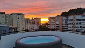 Piscina no terraço com vista para o pôr do sol sobre a paisagem urbana.