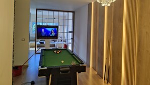 Um quarto com mesa de bilhar, televisão exibindo um programa e um candelabro.