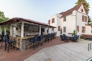 Zona de bar al aire libre con mostrador de piedra y sillas azules, junto a un edificio blanco con detalles rojos y techo rojo.