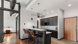 A modern kitchen with a central island, bar stools, dark cabinetry, and pendant lighting.