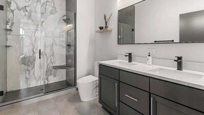 A modern bathroom with a glass-enclosed shower, a large mirror, and a dark-toned vanity with a white countertop.