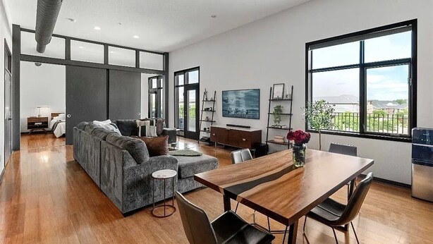 A spacious living room with a sofa, a dining table, and a large window offering a view of the outdoors.