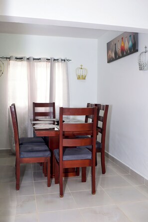 Uma área de refeições com uma mesa e quatro cadeiras, uma cortina, uma decoração com coroa e um quadro com vasos na parede.