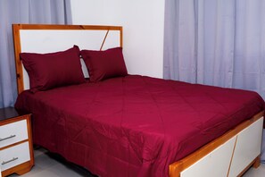 Uma cama com estrutura de madeira e colcha vermelha.