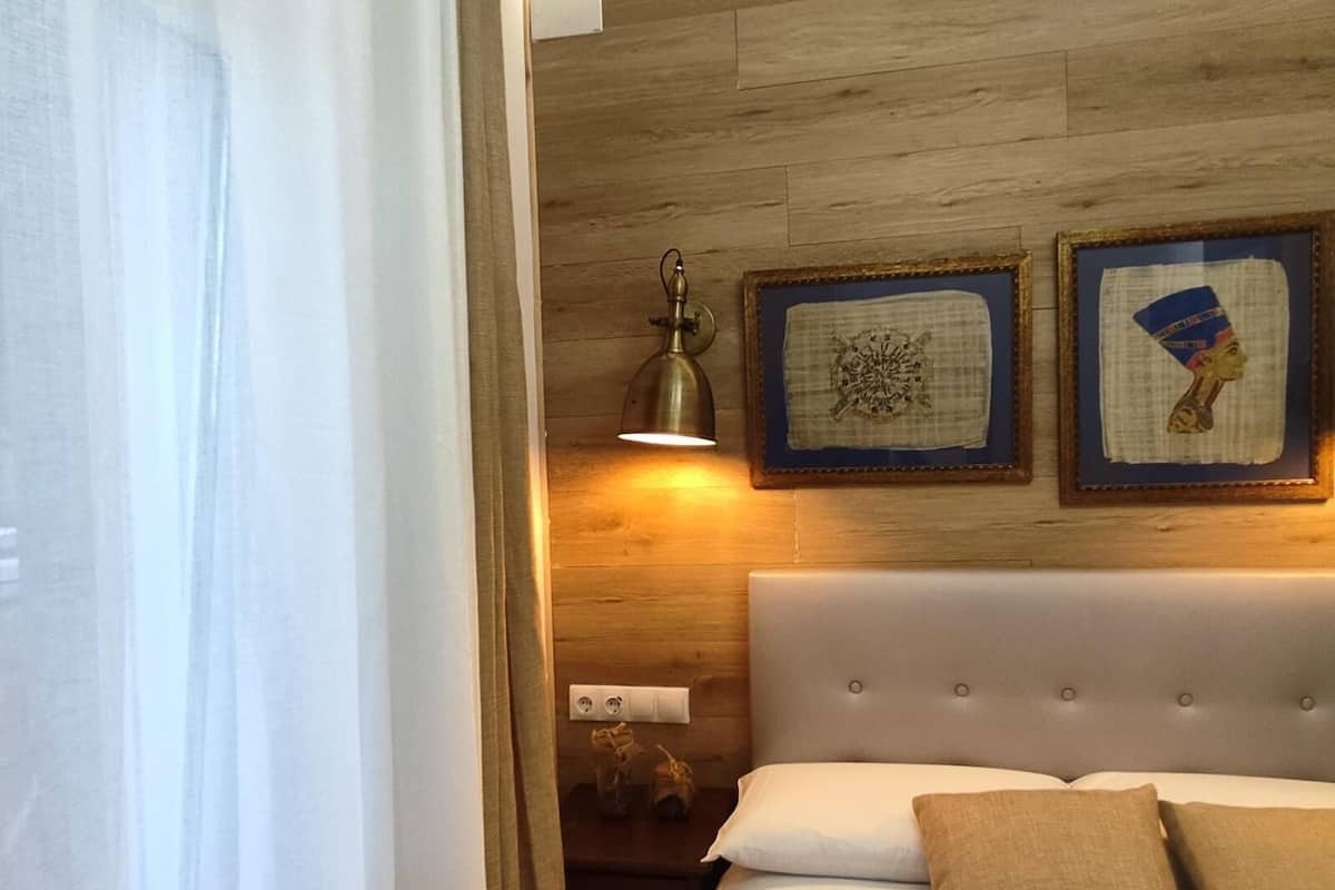 Un dormitorio con una cama, cabecera, lámpara de pared y dos cuadros enmarcados.