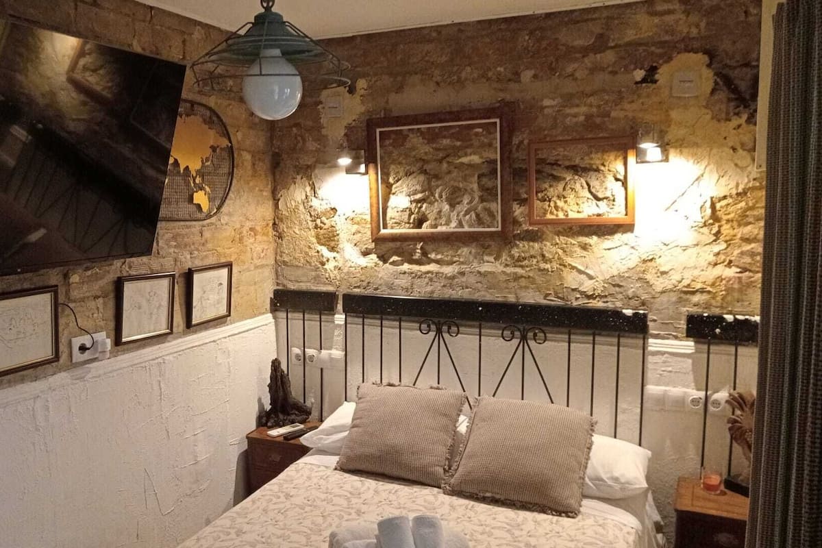 Un dormitorio con pared de piedra, una cama con cabecera y cuadros enmarcados en la pared.