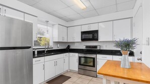 A modern kitchen with white cabinets, stainless steel appliances, and a wooden table.
