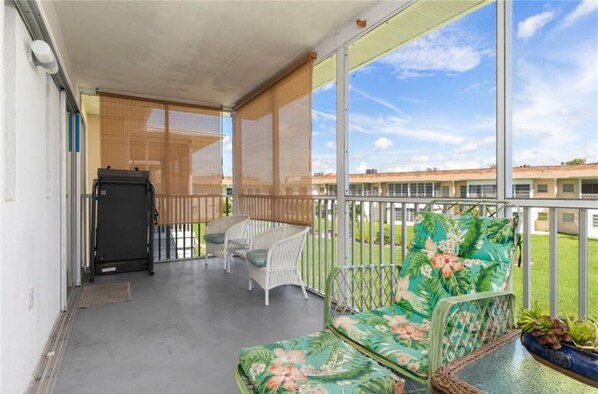 Un balcon donnant sur un immeuble, un canapé, une chaise et une petite table avec une plante.