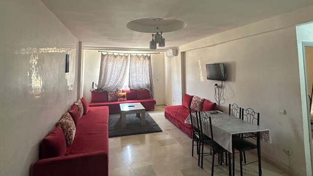 A living room with a red sofa set, a dining table with chairs, and a ceiling fan. - Peaceful retirement near the station (Marrakech)