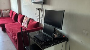 A room with a red sofa, a black desk with a laptop, a TV mounted on the wall, and a ceiling fan. - Peaceful retirement near the station (Marrakech)