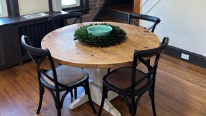 Ein Essbereich mit einem runden Holztisch, vier schwarzen Stühlen, einer grünen Tischdekoration und einer Ziegelwand.