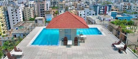 A rooftop swimming pool with a red roof, surrounded by lounge chairs and a table.