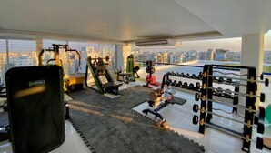 A modern gym with various exercise equipment, large windows, and a city view. - 330sqft 3 Modern Stay with Sauna Pool (Dhaka)